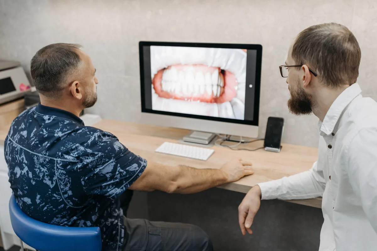 Dos hombres miran juntos la imagen de una sonrisa en la computadora de un consultorio dental