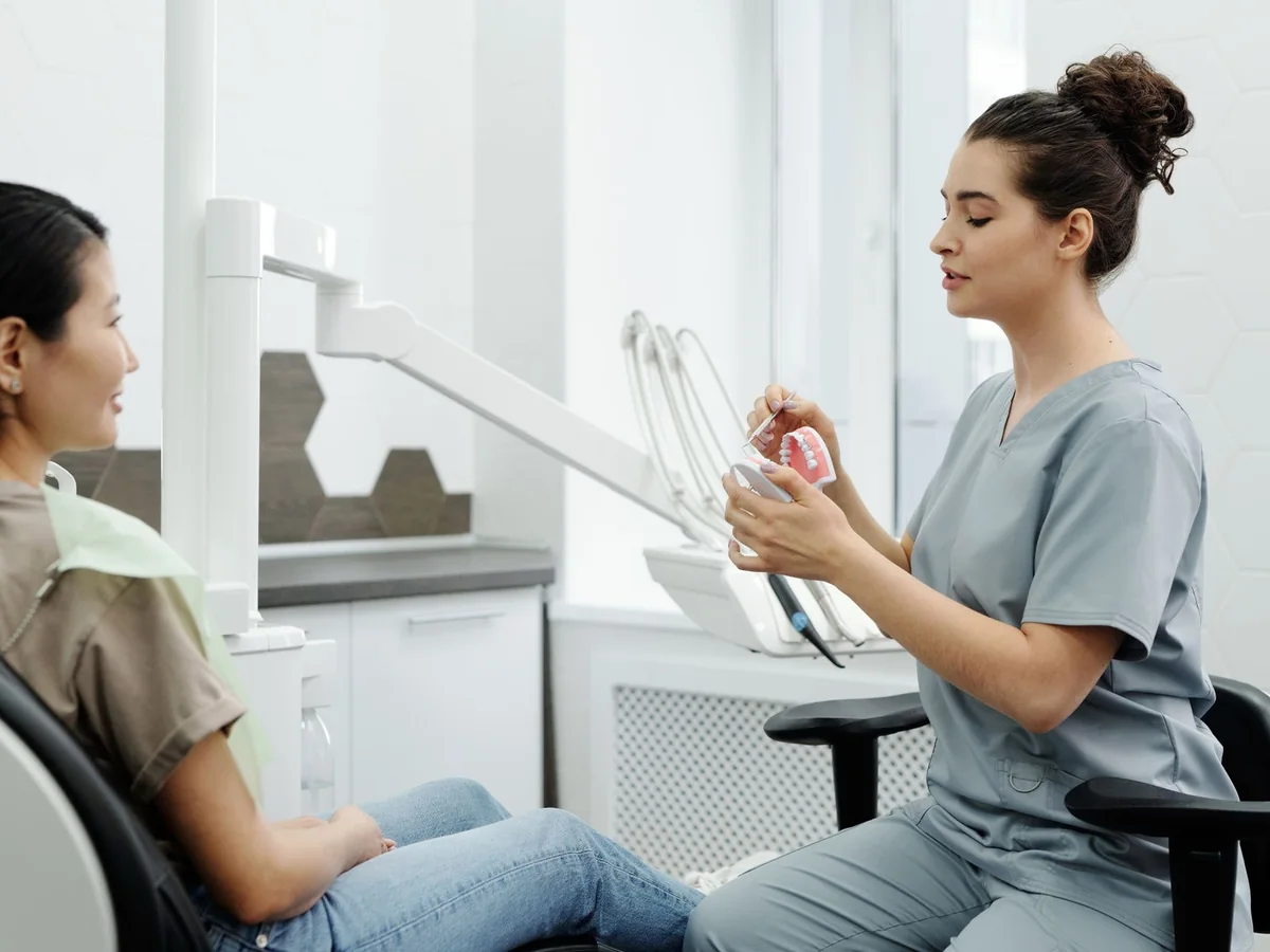 Una odontóloga le explica un tratamiento a una paciente con un modelo dental en la mano